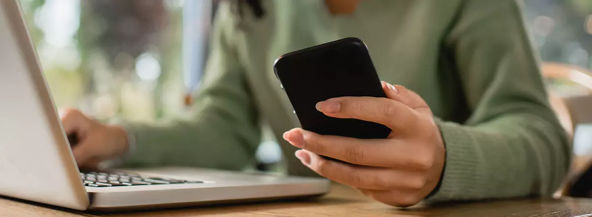 Frau am Laptop mit Smartphone in der Hand