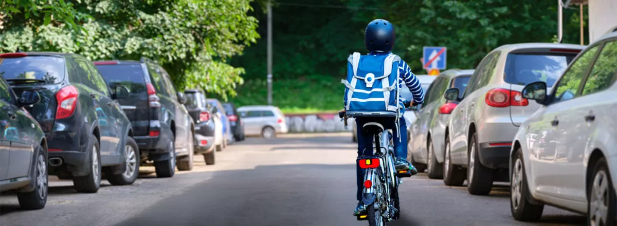 Schulkind fährt mit dem Fahrrad eine Straße mit parkenden Autos entlang